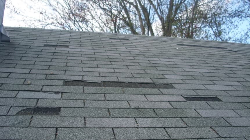 roof-storm-damage A roof with 3 tab shingles that have been damaged by a storm.